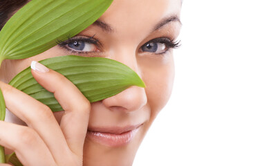 Beauty - the natural way. Closeup portrait of a woman looking at the camera through green leaves.
