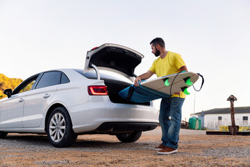 bearded young man taking surfboard out of the car