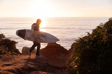 man walking at sunset with a surfboard by the sea