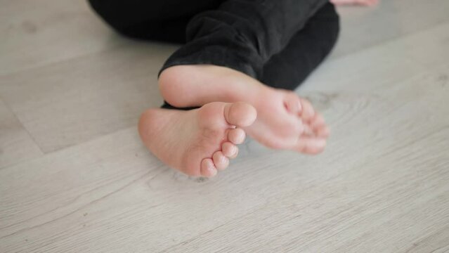 Closeup dirty heels of a child lying on the floor on a white parquet floor in black jeans