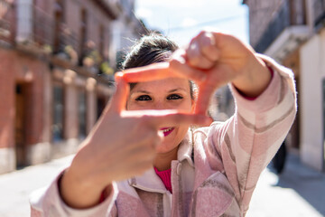 Brunette woman dressing youthfully making gestures with her hands as if she were going to take a photo. Front photo of a young girl wearing a shirt and taking photos in a fictitious way.
