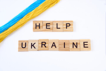 Top view phrase help ukraine is laid out of wooden squares isolated on white background. with flag of ukraine with blue and yellow ribbon. Concept of peace, war in Ukraine