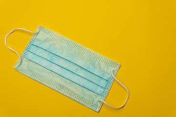 Close-up image of a blue face mask on a yellow background leaving copy space. Sanitary hygiene concept in times of viruses and diseases.