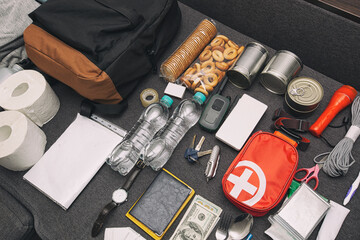 Fototapeta Emergency backpack equipment organized on the table. Documents, water,food, first aid kit and another items needed to survive. obraz
