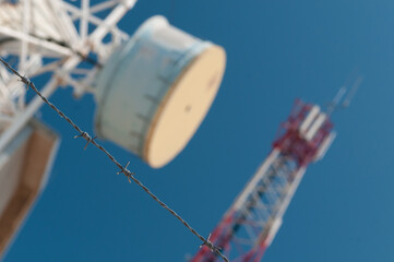 Barbed wire in focus with communication towers and blue sky in background