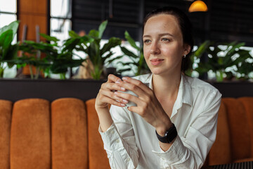 Smiling businesswoman having coffee break in cafe and sitting at table with cup of hot drink while looking away 