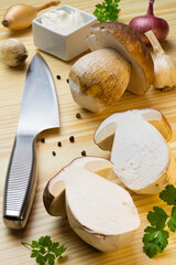 Halved penny bun on cutting board with knife, onions, garlic, black pepper and sour cream. Cep, porcino, boletus edulis