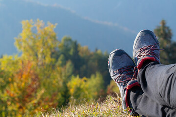 Close-up of legs with hiking shoes. Hiker resting on summit and enjoying spectacular view of autumn forests in background