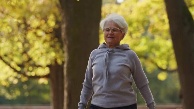 Senior Caucasian woman jumping moving her hands doing sports in the park healthy lifestyle active seniors support concept . High quality 4k footage