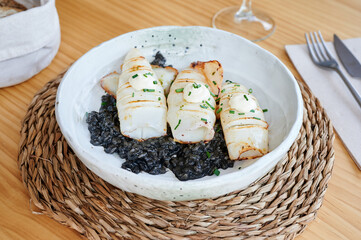 Appetizing black rice and grilled fish garnished with sauce and herbs served in plate on table in restaurant