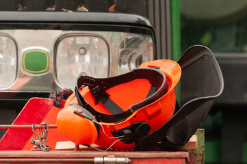 Orange forestry protective helmet with mesh screen visor and earmuffs lying on tractor