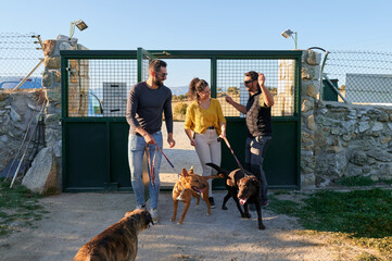 Smiling young couple with their leashed dogs entering kennel greeted by kennel owner