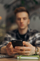 Blurred male freelancer scrolling social media on smartphone and working on online project in cafe 