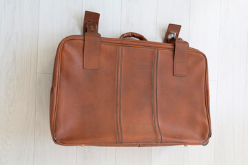 A brown, old, leathery, closed suitcase in retro style is located near the white wall.