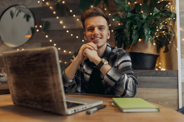 Portrait of smiling male freelancer sitting at table in cafe with laptop and looking at camera 