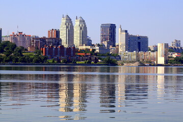 Obraz premium Big city on banks of wide river. Beautiful modern towers, buildings, skyscrapers are reflected in water in summer,Spring. Ukrainian city Dnipro, Dnepropetrovsk, Ukraine