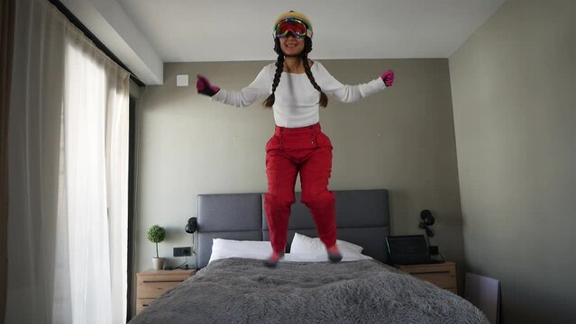 Funny asian girl snowboarder slide on bed in bedroom at home dreaming of trip to ski resort during lockdown due to coronavirus.
