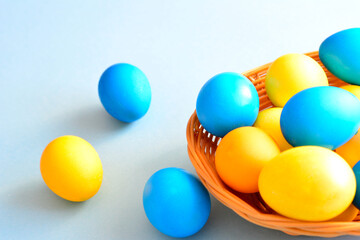 yellow and blue easter eggs in wooden basket on light blue background