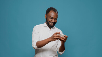 Male gamer playing mobile video games on smartphone in studio, having fun with online gameplay as...