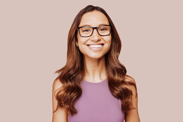 Obraz premium Close up portrait of young happy smiling woman face with eyeglasses, curly hair, wears blue sweater, posing at studio on beige wall background. Cheerful female student. Copy space.