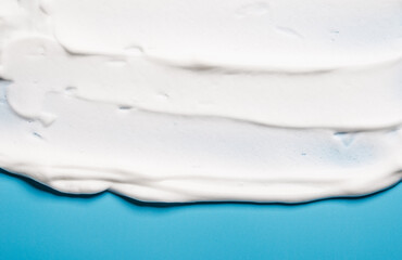 White mousse shaving cream or facial cleanser product or soft soap foam texture background on blue copy space.	