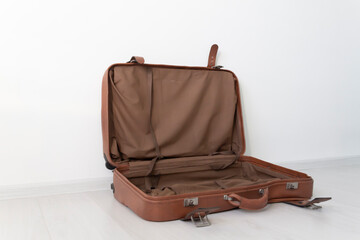 An open, empty, retro leather suitcase near a white wall.