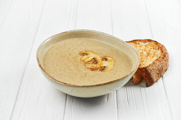 Mushroom cream soup in a plate on a white wooden background