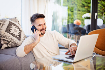 Happy man using mobile phone and laptop while relaxing at home