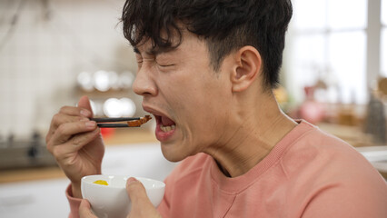 closeup shot of asian male making funny face expression while tasting spicy hot food at dining...