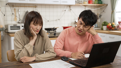 unhappy Chinese married couple calculating budget on calculator in dining room at home. the...