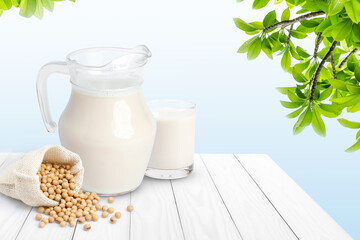 Soy milk in glass pitcher and soybean in sack bag isolated on wooden table with blue background.