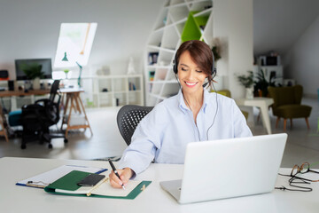 Attractive businesswoman having online meeting while wearing headset and using laptop