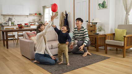 cheerful asian dad, mom and son having fun playing hit the ball game in the living room at home....