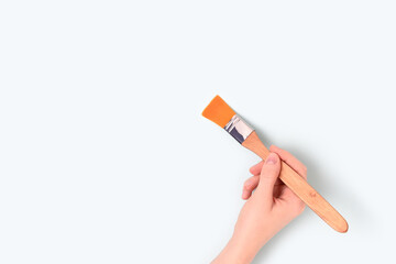 Female hand hold paintbrush on a blue pastel background. Repair concept with copyspace.