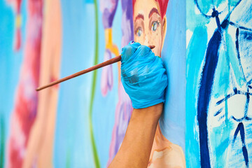 Artist's hand in blue gloves with paintbrush painting colorful picture at outdoor art festival