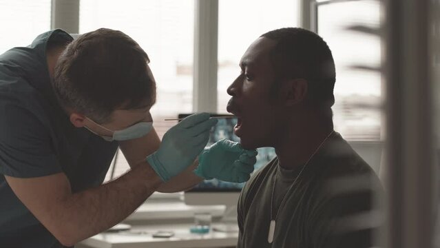 Waist up slowmo of African American army officer in khaki being tested for covid or omicron by male nurse taking mouth swab from him
