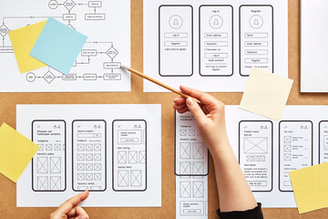 Web UX designer working on mobile responsive website. Flat lay image of numerous app wireframe sketches and user flow over product designer desk. 