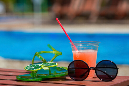 A juicy, summery banner. A glass of freshly squeezed grapefruit juice, flip-flops and glasses on a sun lounger by the pool in the background. The concept of rest, vacation and hot season.