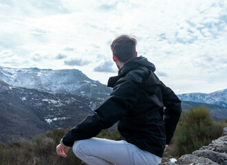 Young man seen from behind sitting in nature watching the landscape