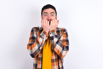 Anxiety - young caucasian man wearing plaid shirt over white background covering his mouth with hands scared from something or someone bitting nails.