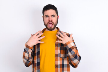 young caucasian man wearing plaid shirt over white background keeps hands on chest feeling shocked...