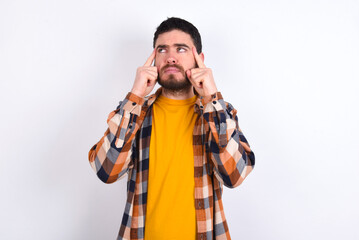 young caucasian man wearing plaid shirt over white background with thoughtful expression, looks away, keeps hand near face, thinks about something pleasant.