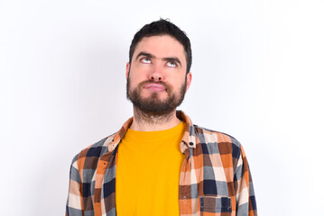 young caucasian man wearing plaid shirt over white background has worried face looking up lips...