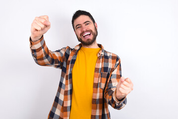 Portrait of charming young caucasian man wearing plaid shirt over white background, smiling broadly while holding hands over her head.  Confidence and relax concept.