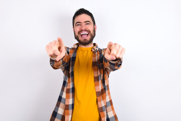 Close-up portrait of surprised young caucasian man wearing plaid shirt over white background pointing with two fingers to the camera saying: I choose you!, looking up with open mouth.
