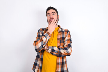 young caucasian man wearing plaid shirt over white background covering mouth with hands scared from something or someone bitting nails