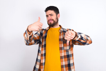 young caucasian man wearing plaid shirt over white background feeling unsure making good bad sign. Displeased and unimpressed.