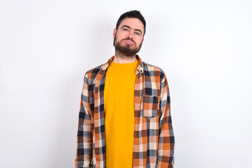 Gloomy, bored young caucasian man wearing plaid shirt over white background frowns face looking up, being upset with so much talking hands down, feels tired and wants to leave.