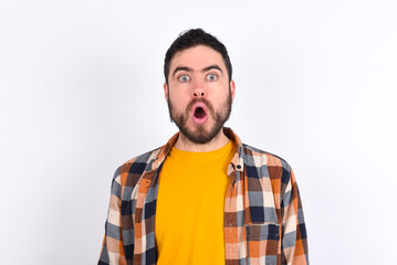 Obraz premium Emotional attractive young caucasian man wearing plaid shirt over white background with opened mouth expresses great surprise and fright, stares at camera. Unexpected shocking news and human reaction.