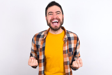 young caucasian man wearing plaid shirt over white background raising fists up screaming with joy being happy to achieve goals.